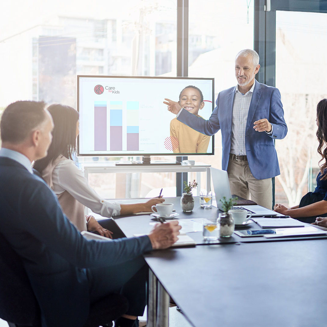 A man presenting information on a TV to a group of people in a room