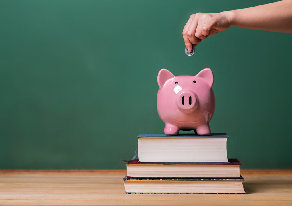 Coin being dropped into a piggy bank resting on a stack of books