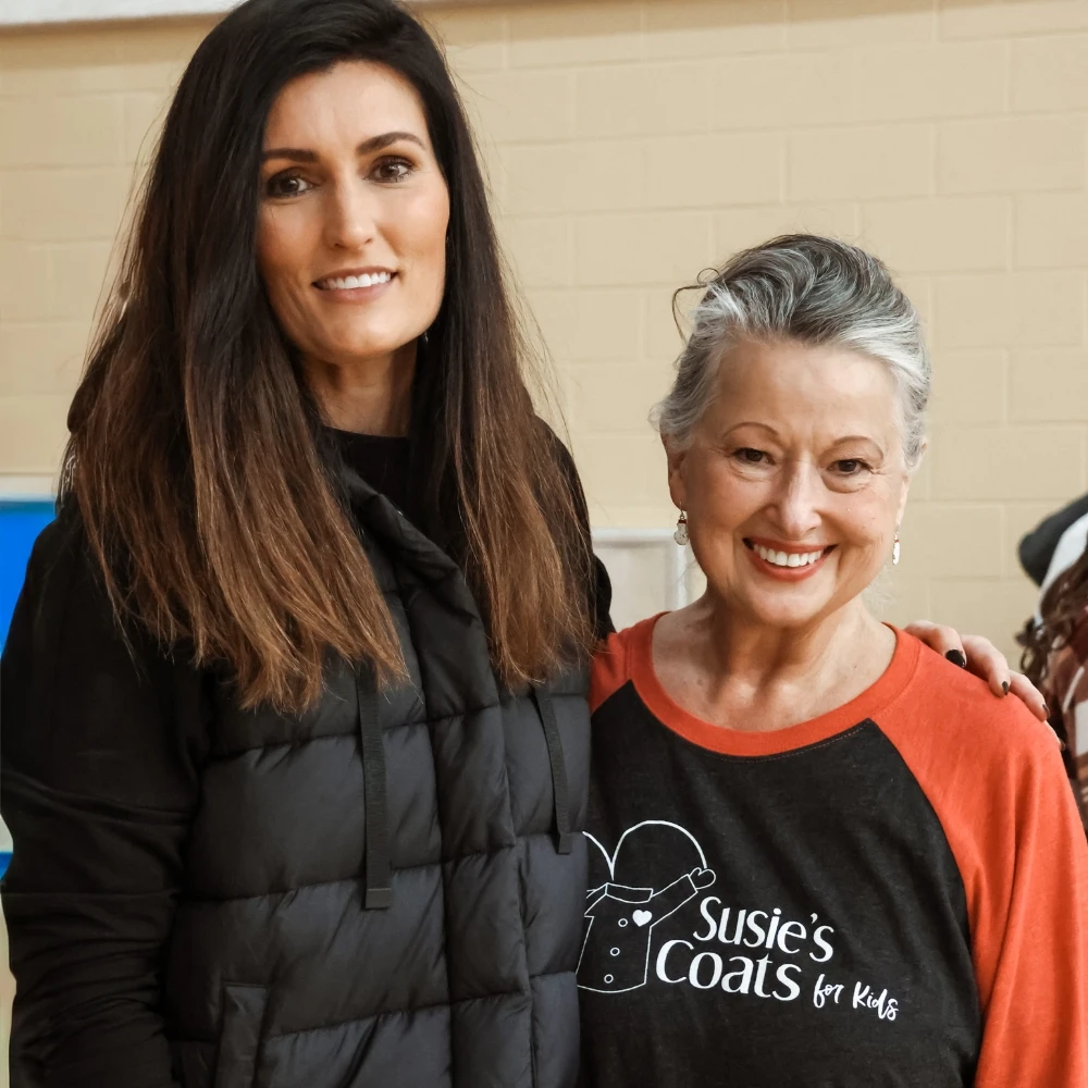 two women standing beside each other and smiling at a volunteer event.