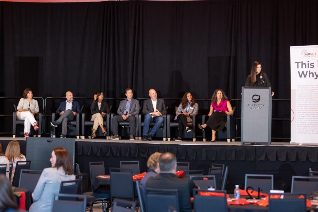 Panelists seated on stage while a speaker addresses the audience from the podium